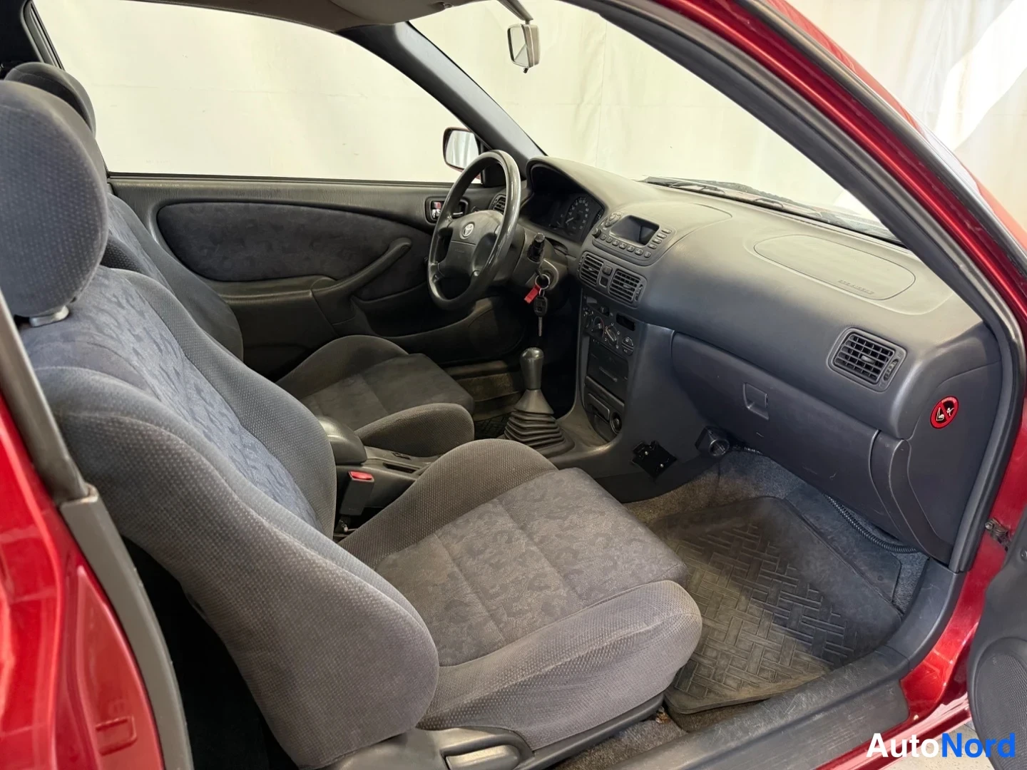 Ohjaamo: Passenger side interior view from open door showing passenger seat, dashboard, glovebox area, and part of rear bench.
