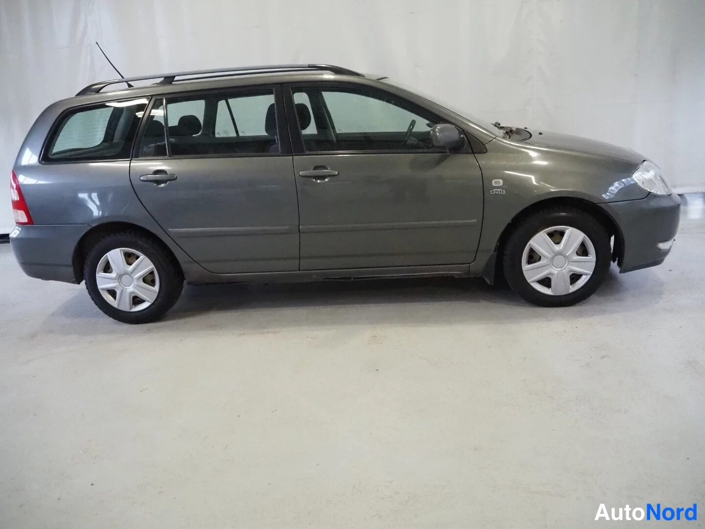Sivulta: Toyota Corolla -farmarin sivuprofiili vasemmalta, autotallitilan vaalealla lattialla.
