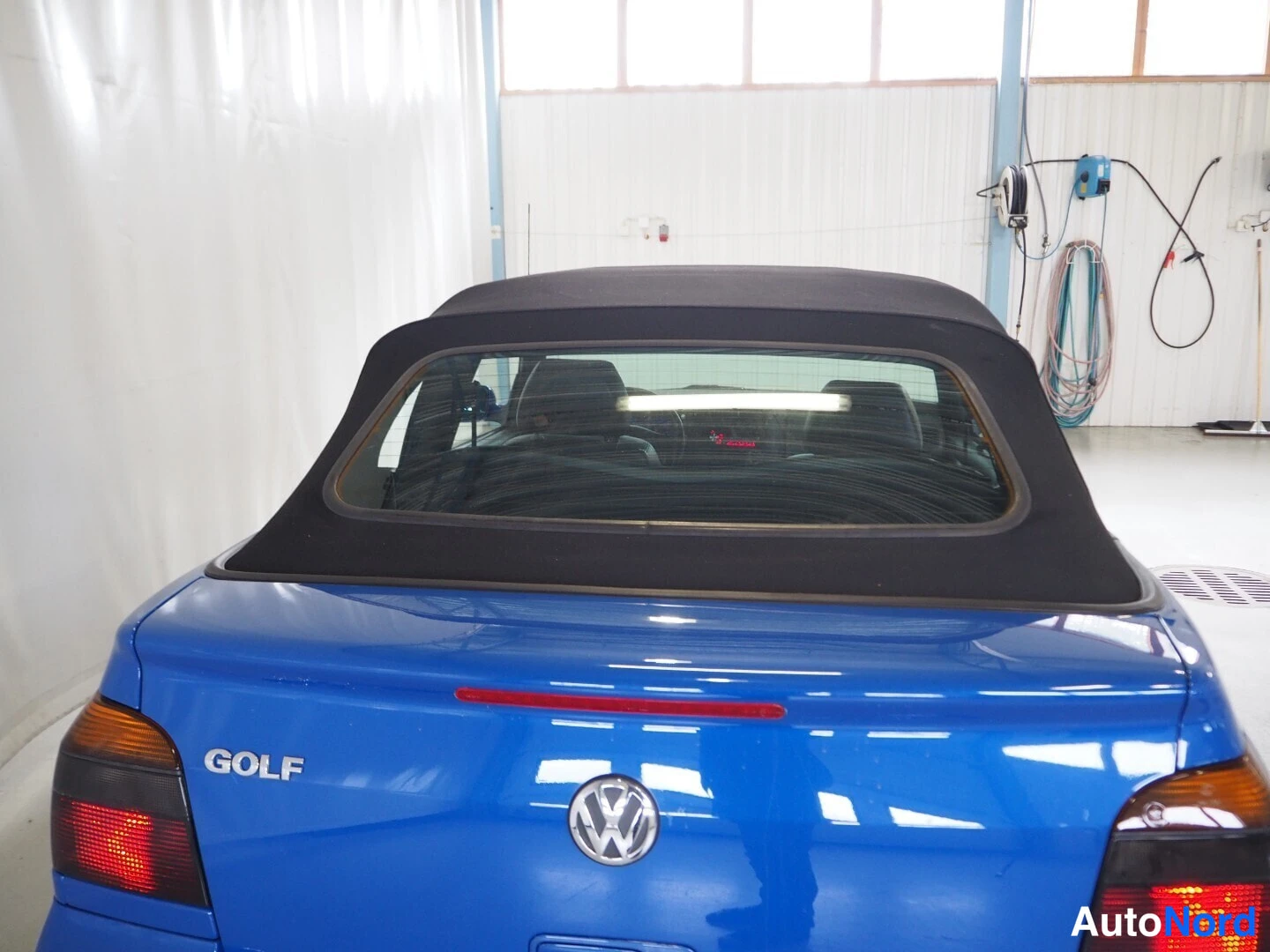 Takaa: Sinisen cabrioletin takaosa suoraan takaa, musta tekstiilikatto, GOLF-merkintä ja Volkswagen-merkki näkyvät.