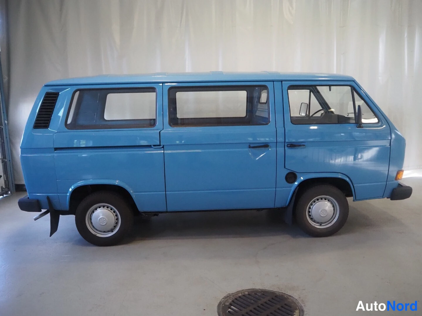 Sivulta: Vaaleansinisen Volkswagen Transporter -pakettiauton kylki kuvattuna sivulta oikealta, liukuriippuva takaportaali ja pyöränkannattimet.