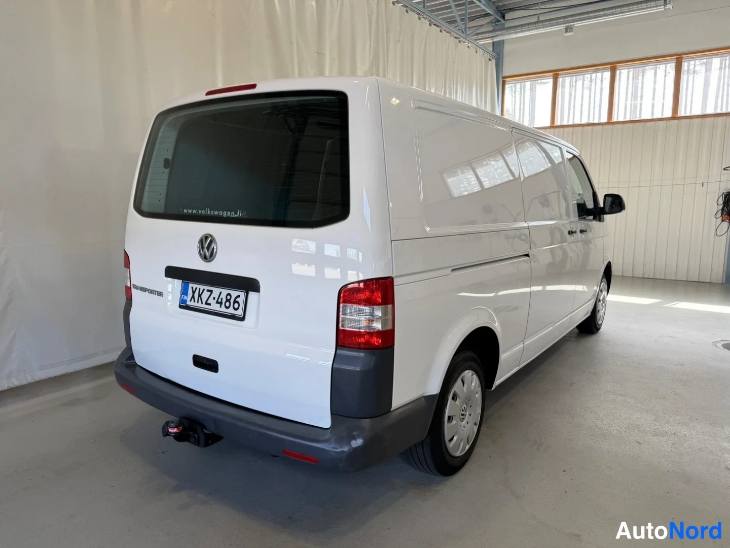 Takaviisto: Valkoinen Volkswagen Transporter -pakettiauto takakanavalta vasemmalta, rekisteritunnus ja Transporter-teksti takaluukussa.