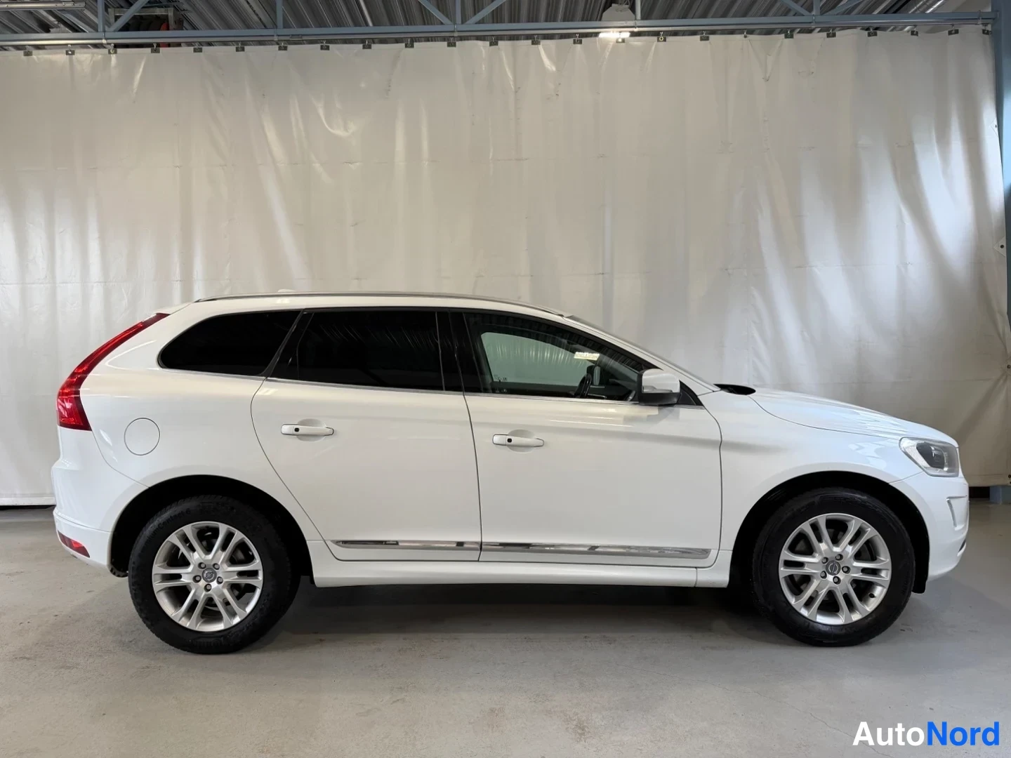 Sivulta: Valkoisen Volvo XC60:n kylki sivusuunnassa sisätiloissa, auton keula osoittaa oikealle.