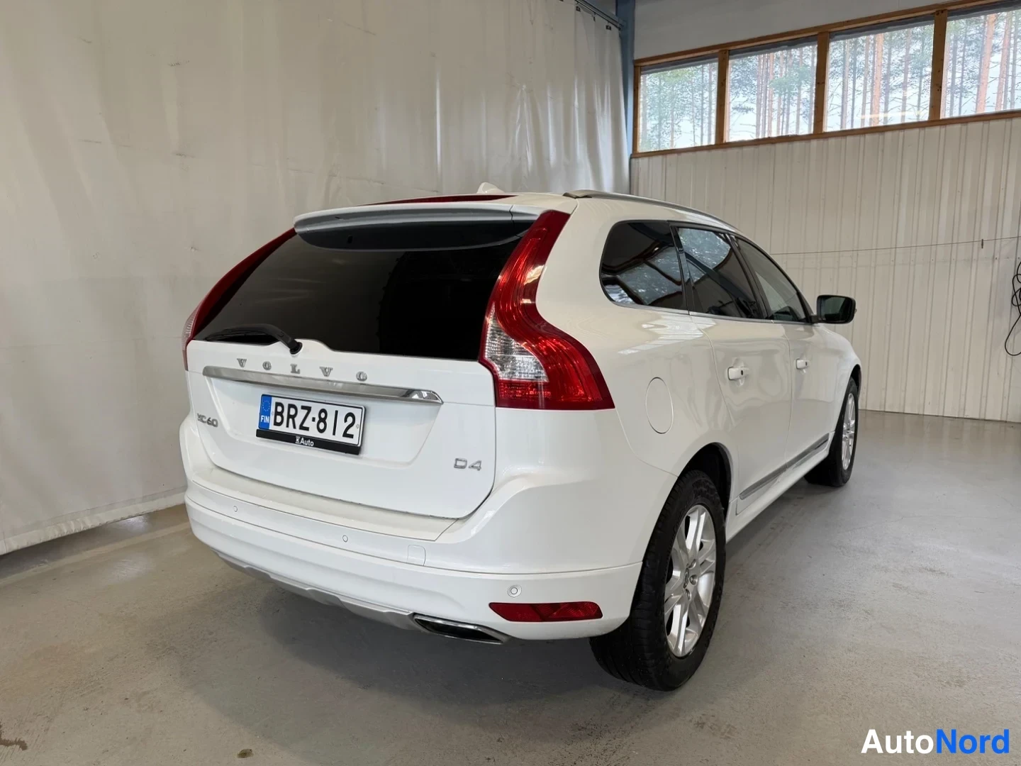 Takaviisto: Valkoisen Volvo XC60:n takapää ja vasen kylki kulmasta sisätiloissa, rekisterikilpi ja D4-merkintä takaluukussa.
