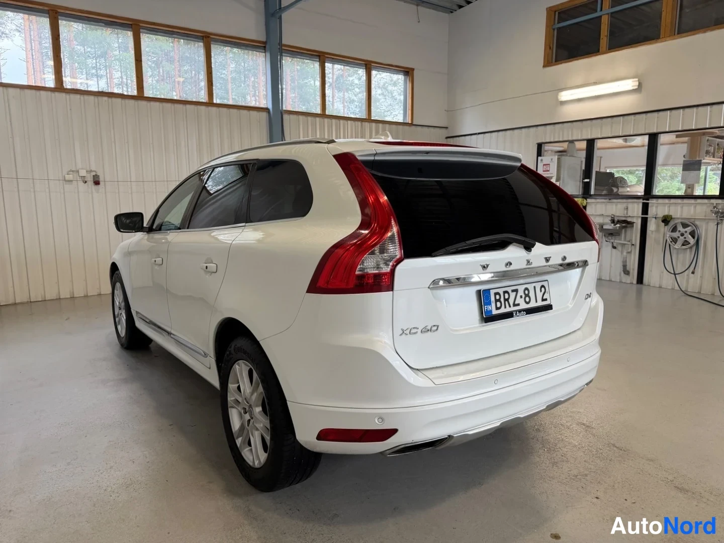 Takaviisto: Valkoisen Volvo XC60:n takapää ja vasen kylki kulmasta hallissa, takaluukussa XC 60 -merkintä ja rekisterikilpi.
