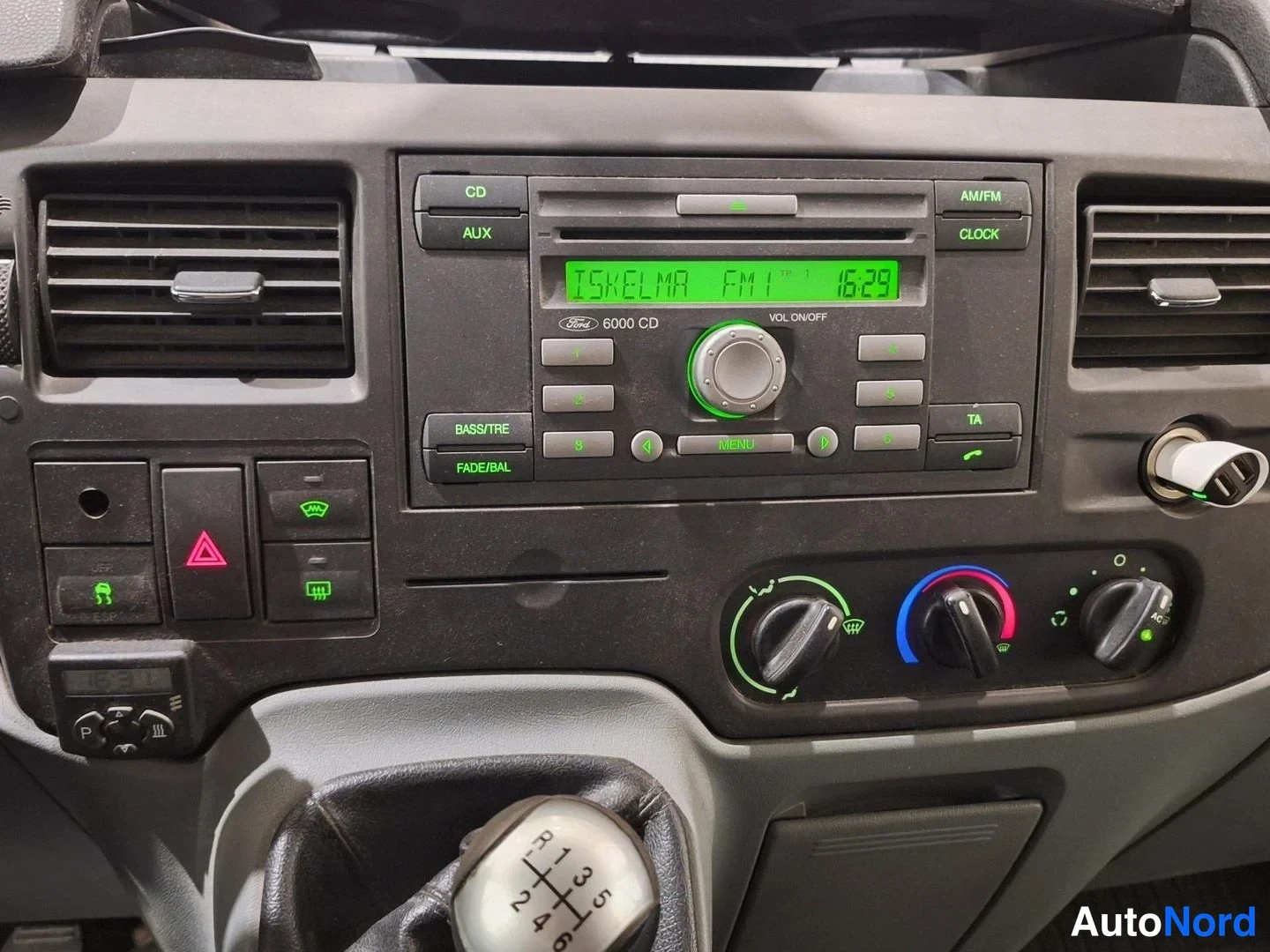 Muu: Kojelaudan keskusta: Ford 6000 CD -radionäyttö tekstillä ISKELMA FM1 16:29, CD/AUX-napit, lämmityksen säätönupit ja manuaalivaihteen keppi.