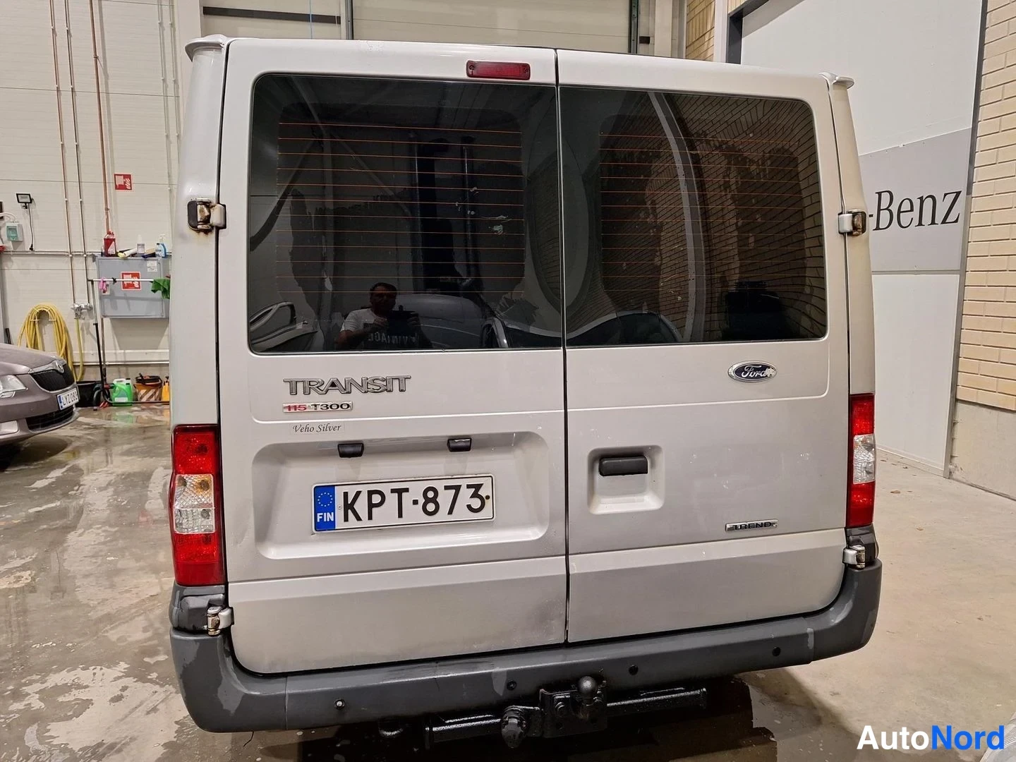 Takaa: Ford Transit -pakettiauton takaosa riippukuormaimella, rekisterikilpi, hopeisenharmaa kori.