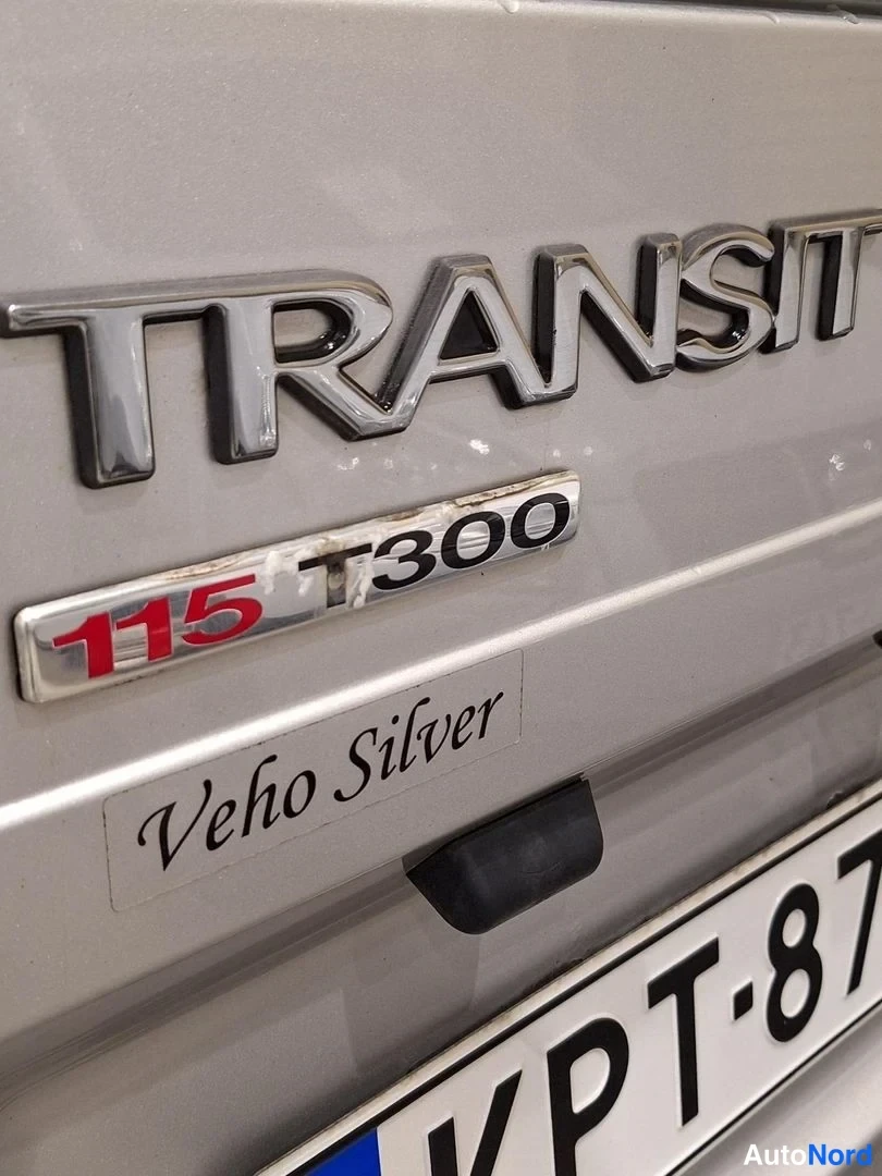 Muu: Lähikuva Ford Transitin takaluukun embleemeistä: 'TRANSIT', '115 T300' ja koristemerkintä 'Veho Silver'.