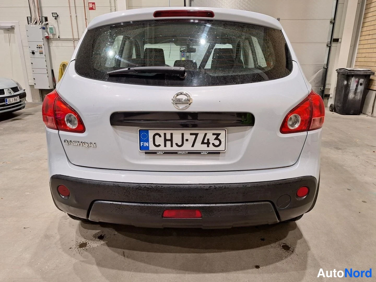 Takaa: Auton takaosa suoraan takaa: valkohopea Nissan Qashqai, rekisteritunnus, punaiset takavalot ja musta puskuri.