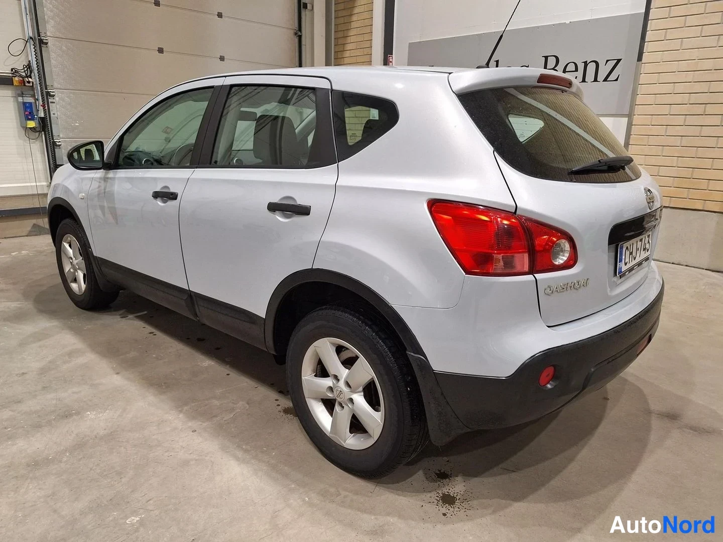 Takaviisto: Hopea Nissan Qashqai takaviistolta oikeaa sivua ja takaosaa näkyy, mustat muovilistat ja hopeavanteet.
