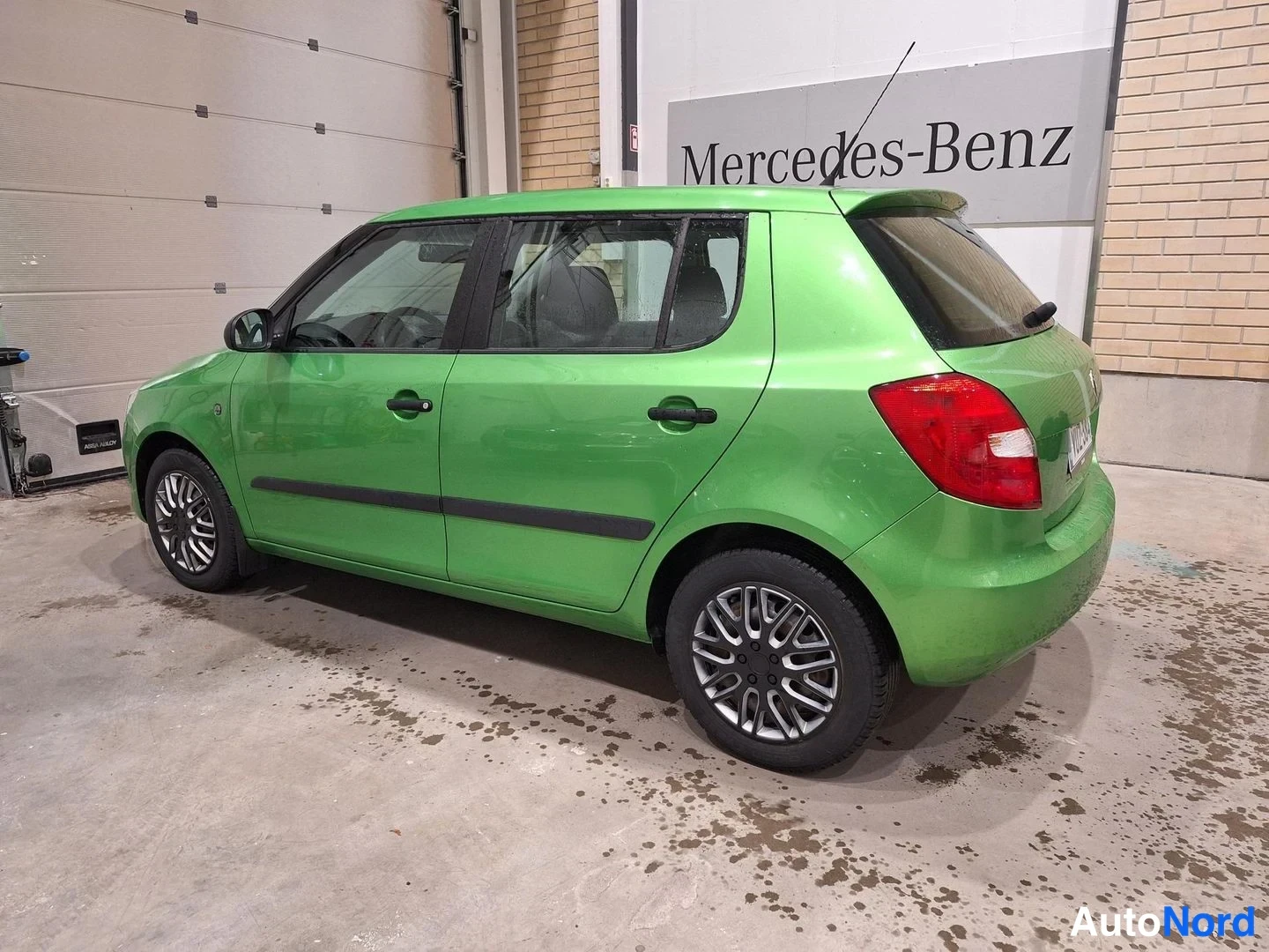 Takaviisto: Vihreä viistoperäauto sivulta takaa katsottuna hallissa, taustalla Mercedes-Benz-kyltti.