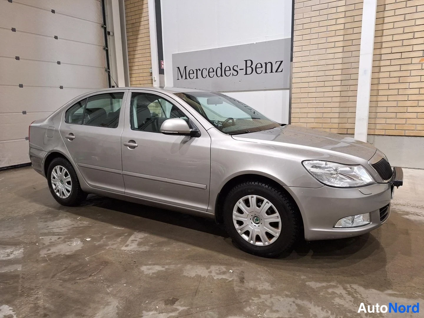 Etuviisto, nokka oikealle: Harmaanbeige Škoda Octavia -sedan etuosa kolmesta neljästä näkyvissä sisätilassa, keulajälki oikealla.