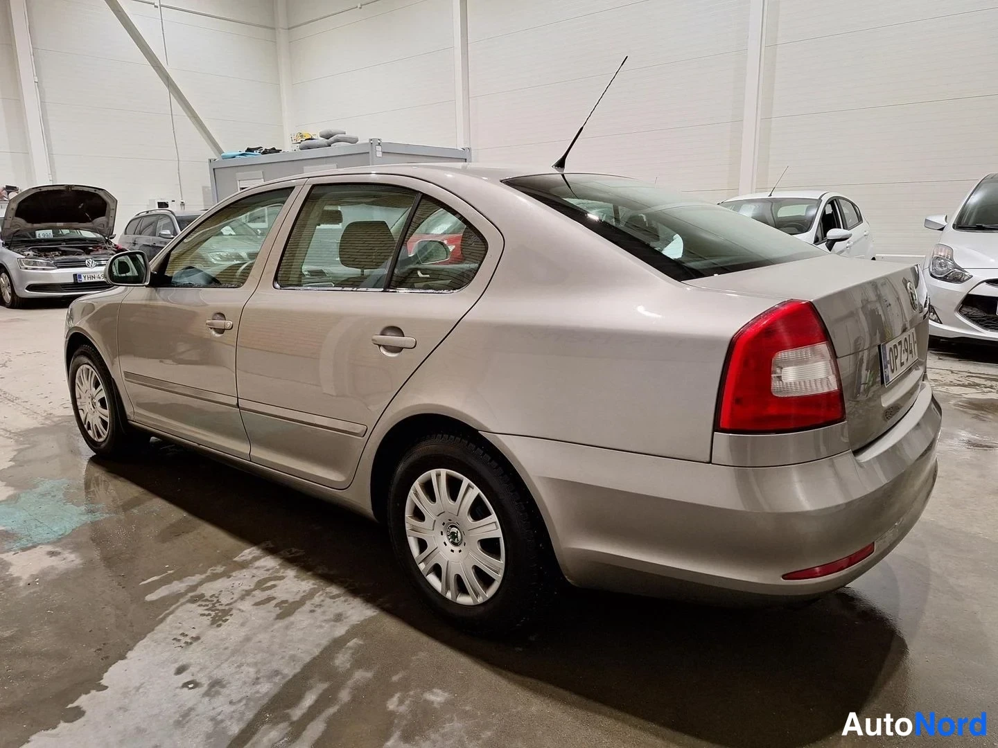 Takaviisto: Auton takaosa ja vasen kylä kolmannesnäkymässä: beigenharmaa Skoda Octavia -sedan, -kilpi takaluukussa.