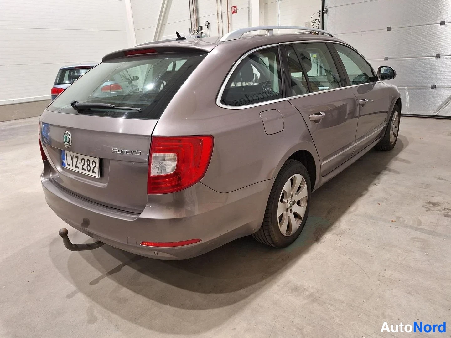 Takaviisto: Auto kolmisivukulmasta takaa vasemmalta; takapää, peräluukun Superb-teksti, vetokoukku ja kattokaiteet näkyvät.