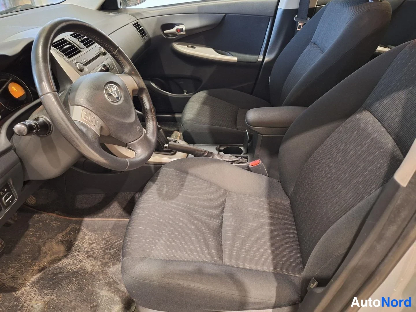 Muu: Auton sisusta: kuljettajan istuin ja ohjauspyörä Toyota-logolla, mustat kankiistuimet, keskikonsoli ja kojelauta.