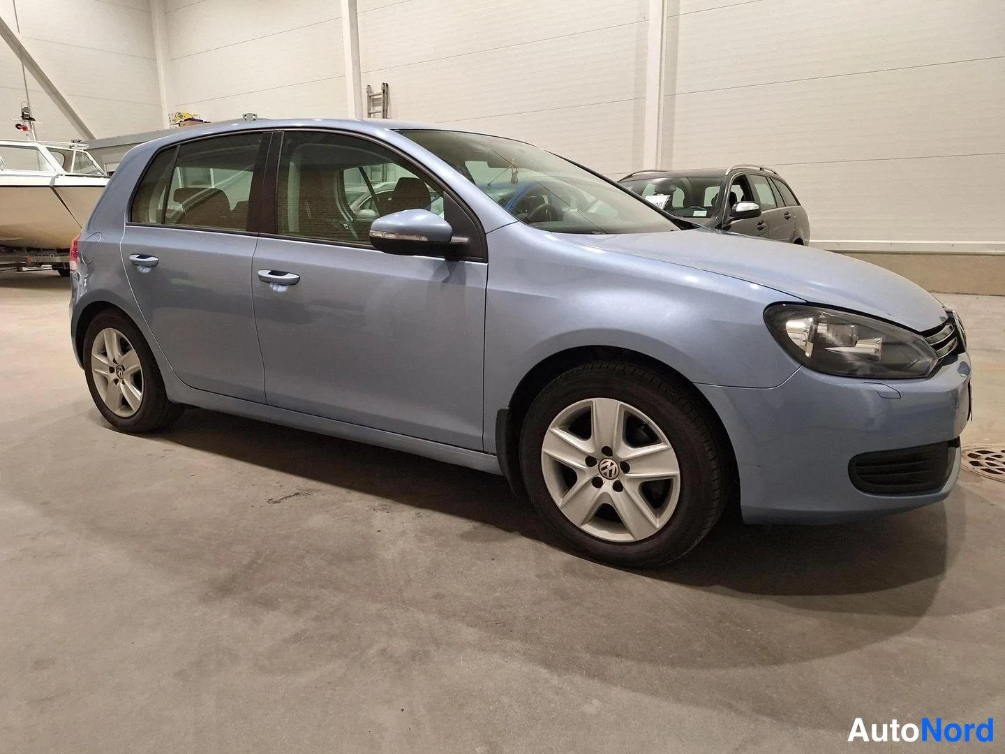 Etuviisto, nokka oikealle: Volkswagen Golf viistoperä etuviistosta oikealta, vaaleansininen kori ja hopeanväriset vanteet hallissa.