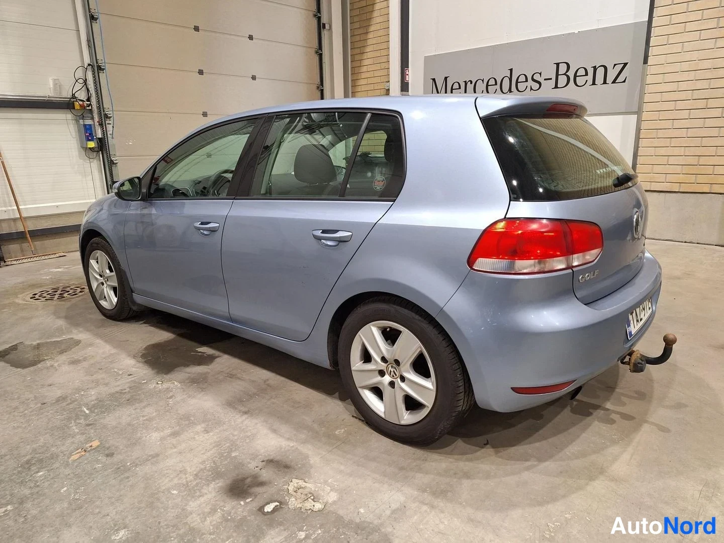 Takaviisto: Valkoharmaan sininen Volkswagen Golf viistoperä kuvattu takaviistosta hallissa; takaosassa -rekisterikilpi ja irrotettava vetokoukku.