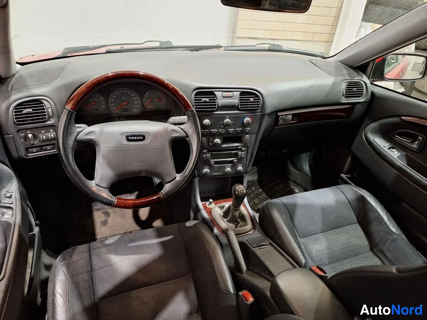Yksityiskohta: Volvo S40:n sisätila etupenkiltä kuvattuna: kirkaspuinen ohjauspyörä, tumma kojelauta ja manuaalivaihteisto.
