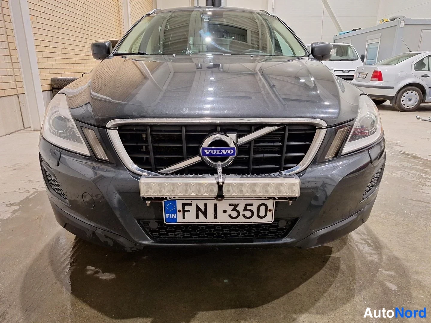 Edestä: Volvo XC60:n etupään suorakuva sisätilassa, rekisteritunnus, eteen kiinnitetty LED-valo.