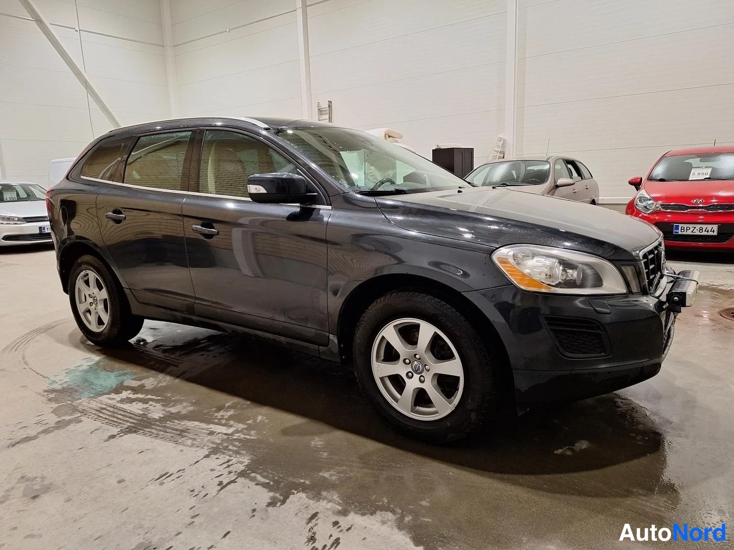 Etuviisto, nokka oikealle: Volvo XC60 kolmivartalokuva etuvasemmalta, tummanharmaa crossover sisähallissa.