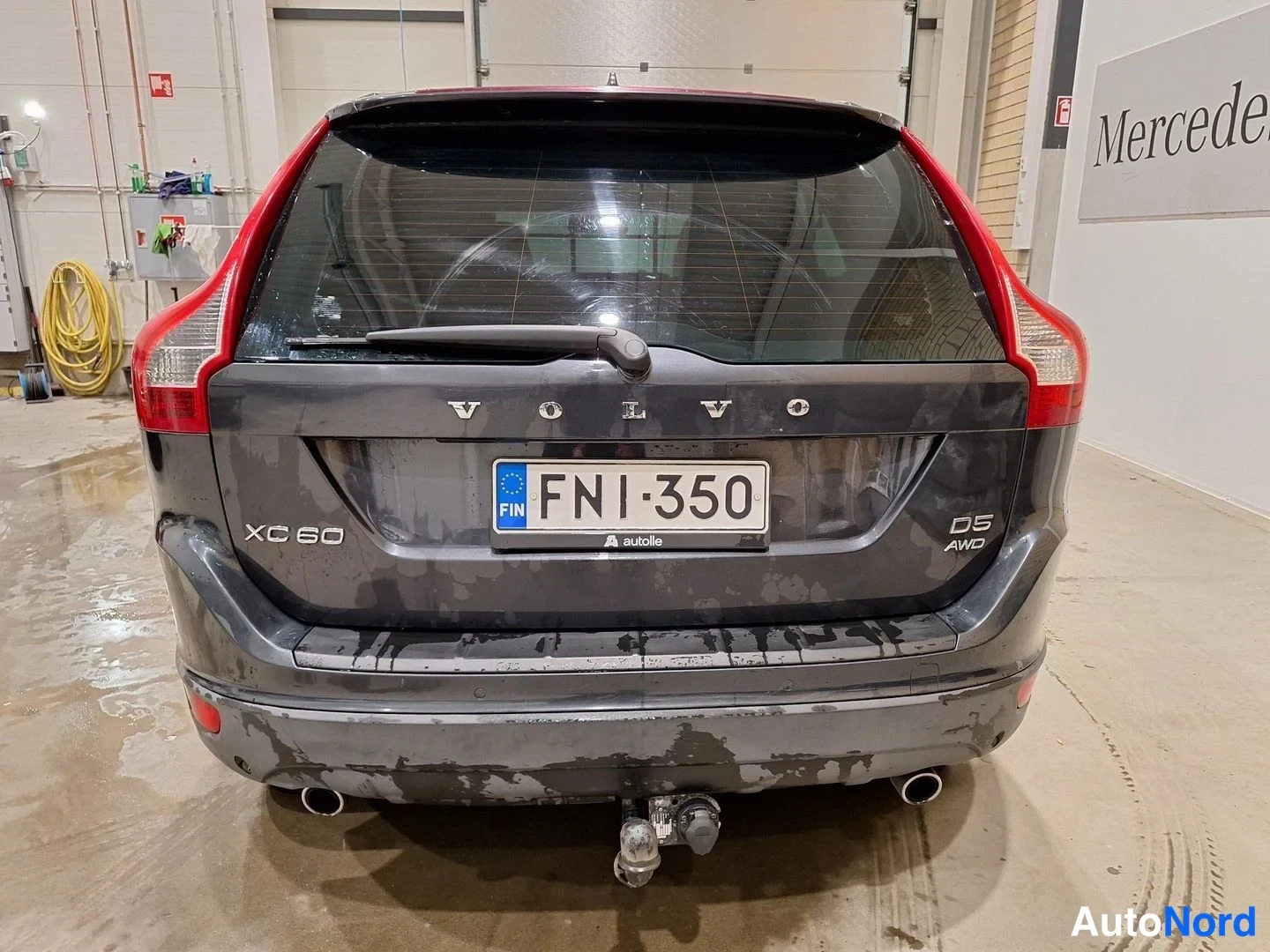 Takaa: Auton takaosa suoraan takaa: tummanharmaa farmari, rekisterikilpi, VOLVO- ja XC60-merkinnät, D5 AWD-tunnus, vetokoukku takapuskassa.