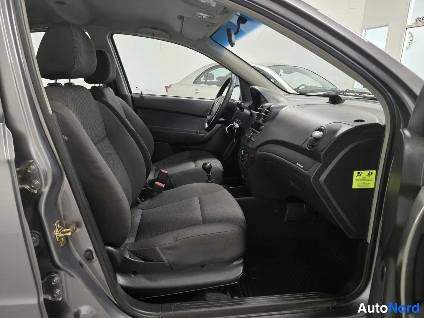 Etuviisto: Chevrolet Aveon etuistuimet ja kojelauta avatusta oikeasta etuovesta kuvattuna; kuljettajan oven takana näkyy toinen ajoneuvo.