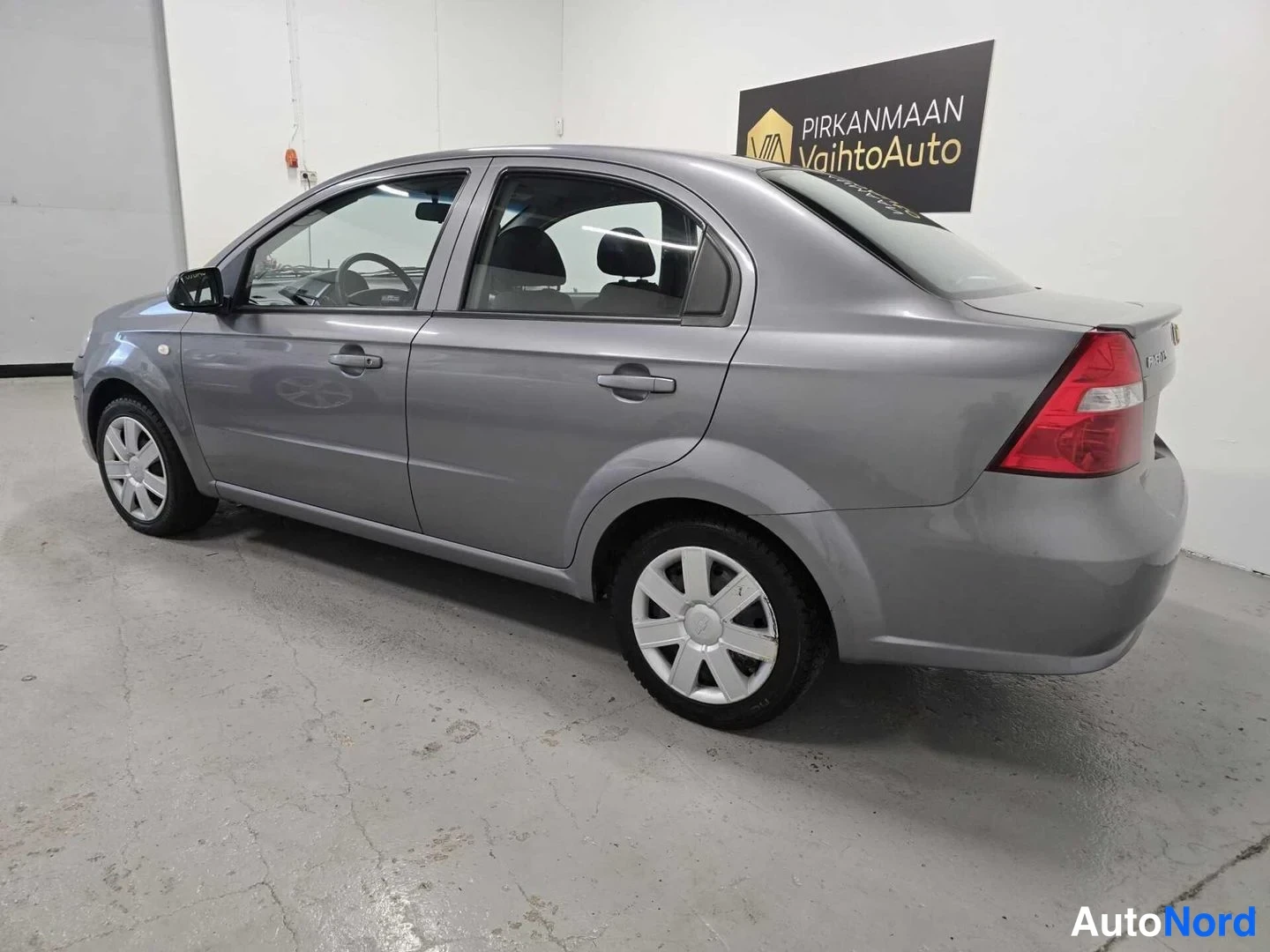 Takaviisto: Chevrolet Aveo -sedanin takakulma lähikuvassa; vaaleanharmaa koripinta, punainen takavalo ja takaovan kahva ovat näkyvissä.