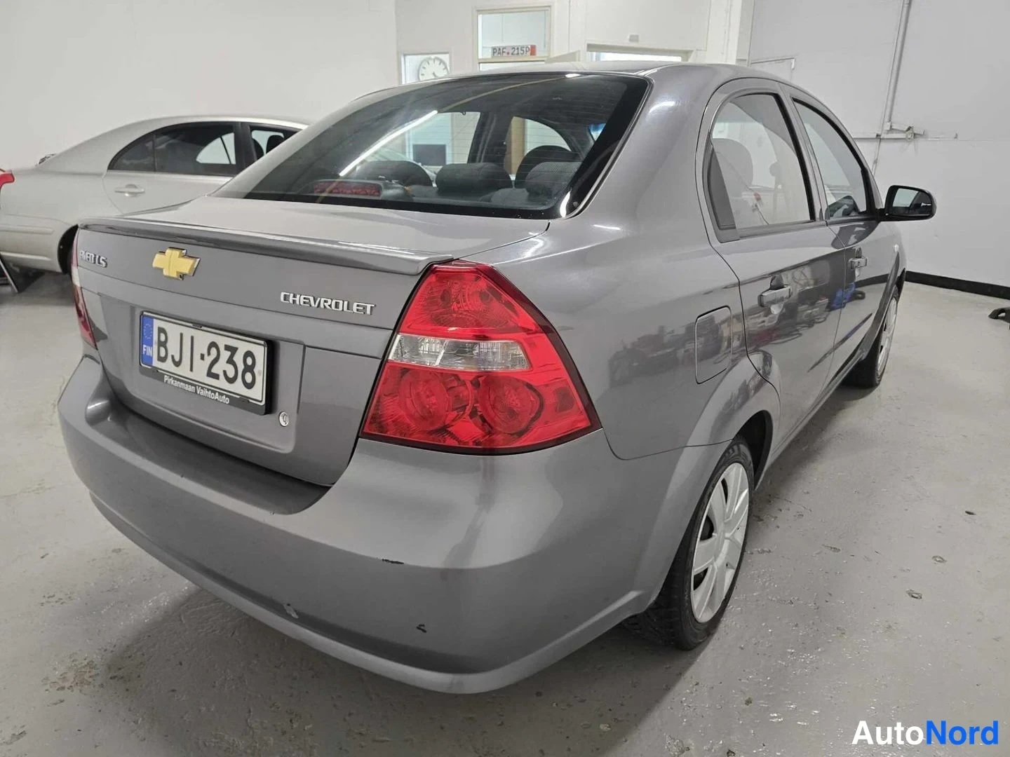 Takaviisto: Chevrolet Aveo -sedanin takapuoli suoraan takaa kuvattuna; kannessa Chevrolet-merkki, TAILGATE-teksti ja rekisterikilpi, punaiset takavalot näkyvät.