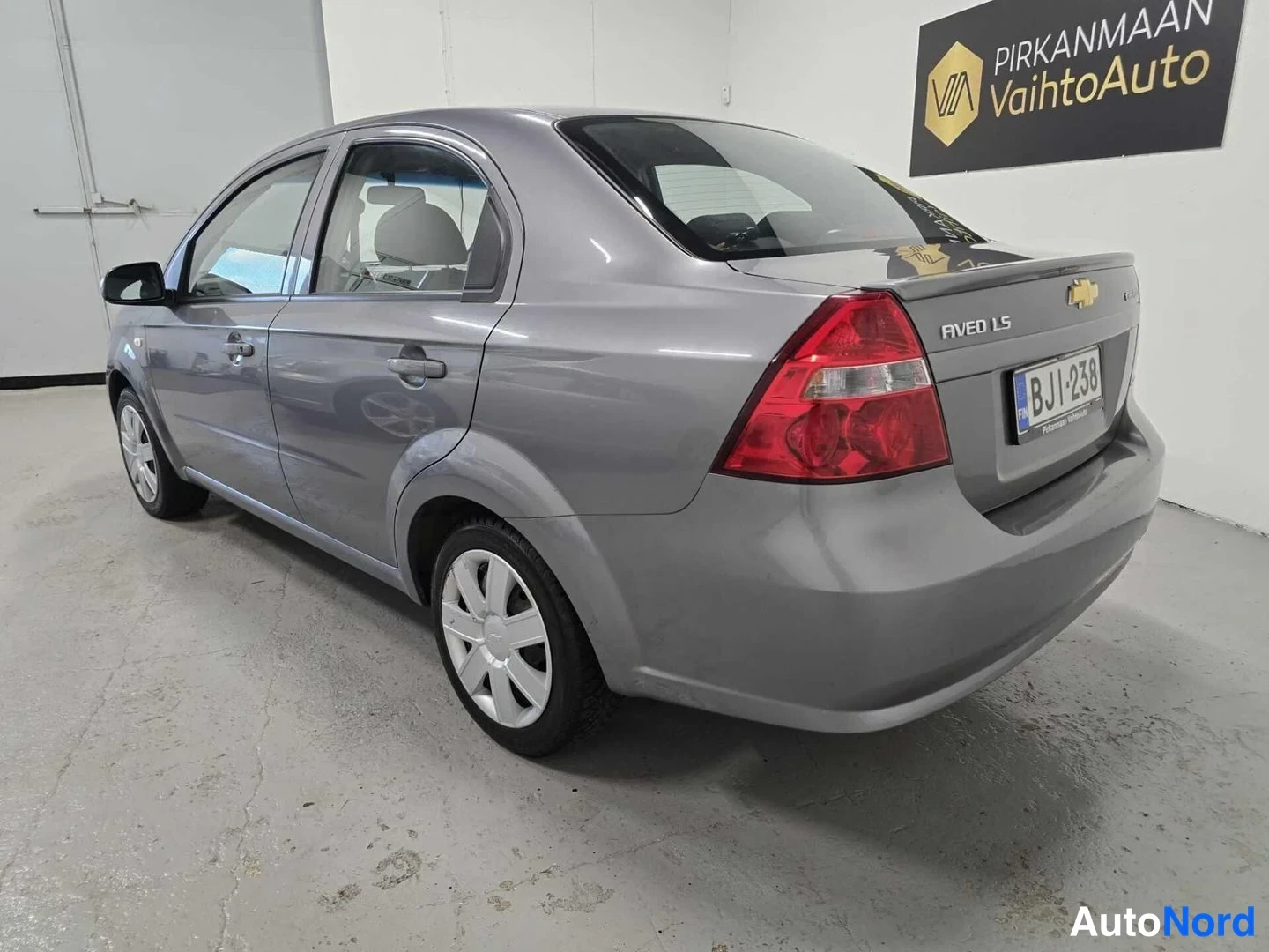 Takaviisto: Chevrolet Aveo -sedanin takakolmasosa sisätiloissa; harmaassa korissa näkyvät takavalo, AVEO LS -merkintä ja rekisterikilpi.