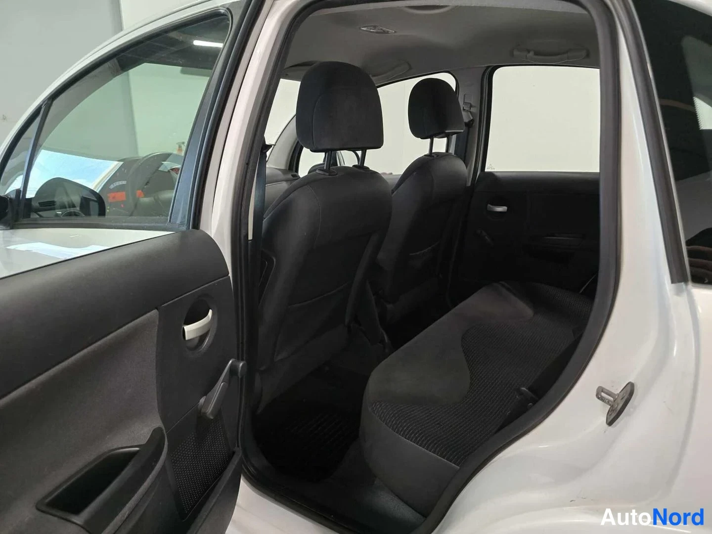 Sivulta: Auto näkyy avoimesta takaovesta: tummat istuimet ja takapenkki sisätiloissa, korin pintaa valkoinen.