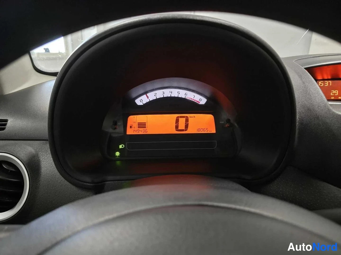Yksityiskohta: Mittariston lähikuva: oranssi näyttö näyttää 143436 km kokonaislukumatkan, 18065 matkamittari- arvon ja 0 km/t nopeuden.