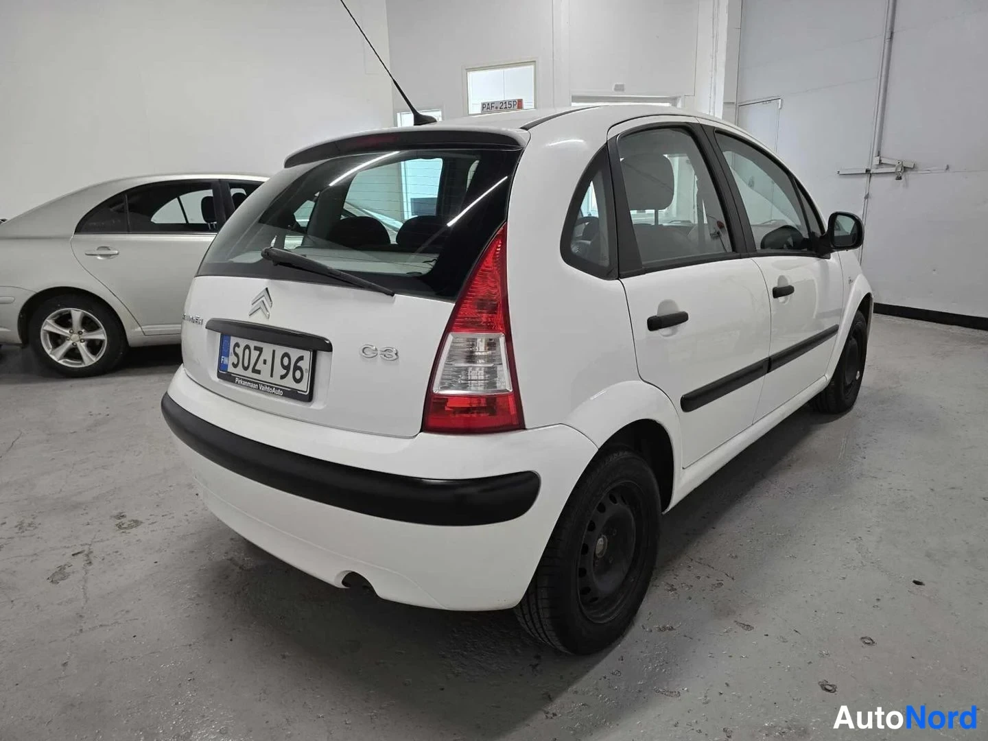 Takaviisto: Citroën C3:n takakulma valkoisena, rekisterikilpi, varapyörä takana mustalla peltivanteella, autotallissa.