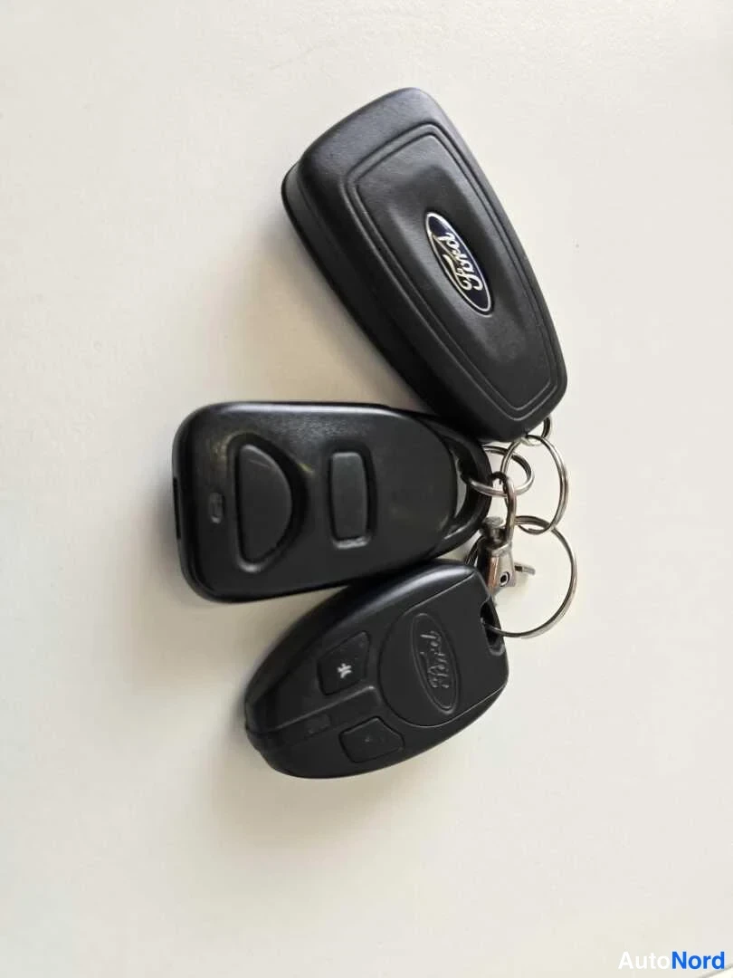 Yksityiskohta: Kolme Ford-merkkistä avainnapia ja kauko-ohjainta avainnipussa vaalealla pöydällä.