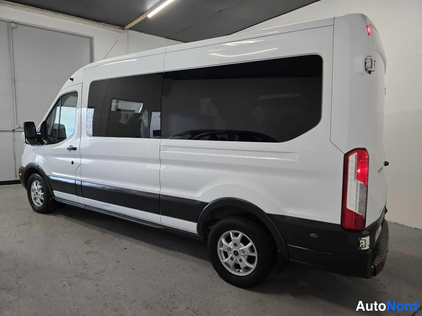 Takaviisto: Valkoinen Ford Transit -pakettiauto kulmasta takaa oikealta kuvattuna; takaosa ja vasen kylki näkyvät, tummat ikkunat ja takavalot tunnistettavissa.