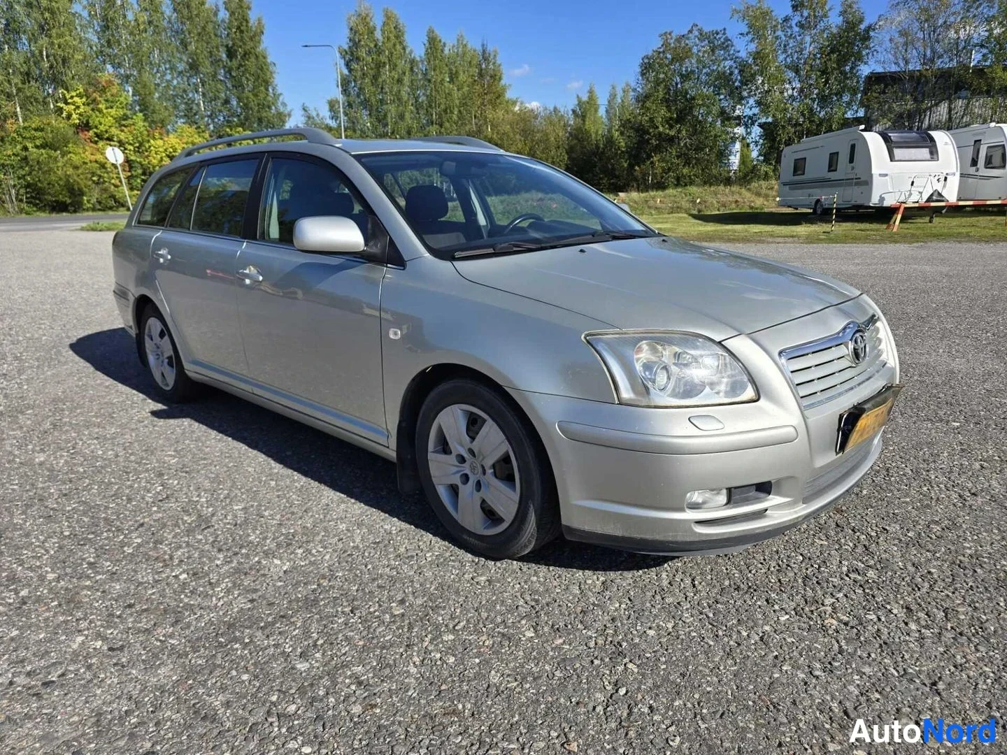 Etuviisto, nokka oikealle: Toyota Avensis -farmari kolmannelta keula oikealle kääntyneenä, hopeanvärinen kori, kattokaiteet ja xenon-tyyppiset etuvalot näkyvissä.