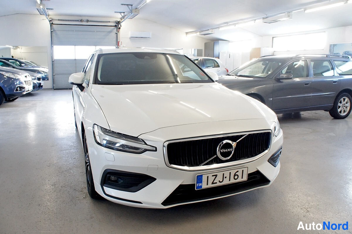 Etuviisto, nokka oikealle: Valkoisen Volvo V60 -farmarin etupää ja vasen kylki kolmanneltaseisommasta, rekisterikilpi.