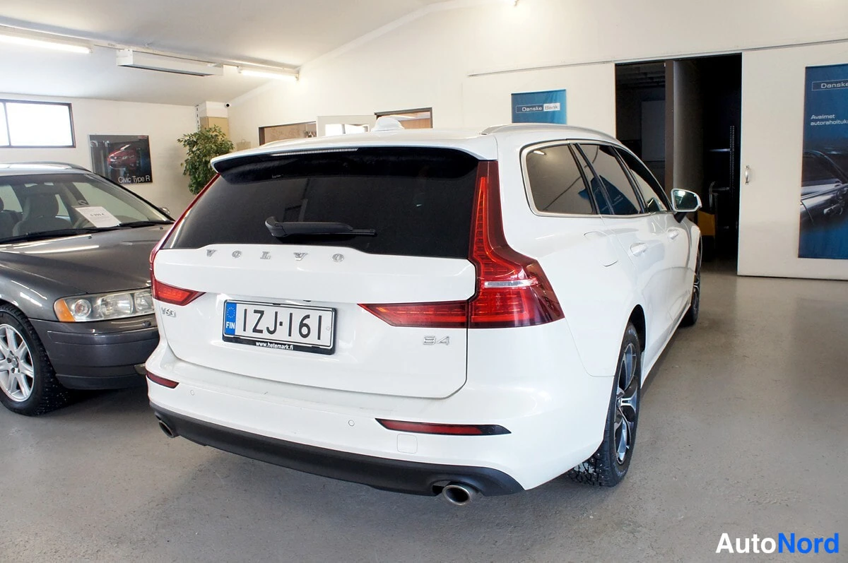 Takaa: Valkoisen farmariauton takaosan näkymä sisätiloissa: VOLVO-teksti takaluukussa, punaiset takavalot ja rekisterikilpi 1ZJ-161.