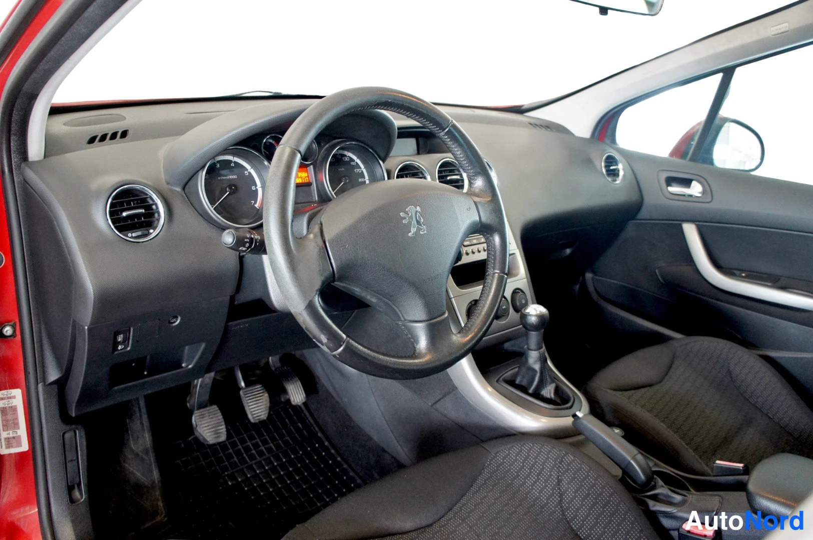 Muu: Kuljettajan näkymä: Peugeot-ohjauspyörä, mittaristo, manuaalivaihteisto ja radiopaneeli mustassa kojelaudassa.