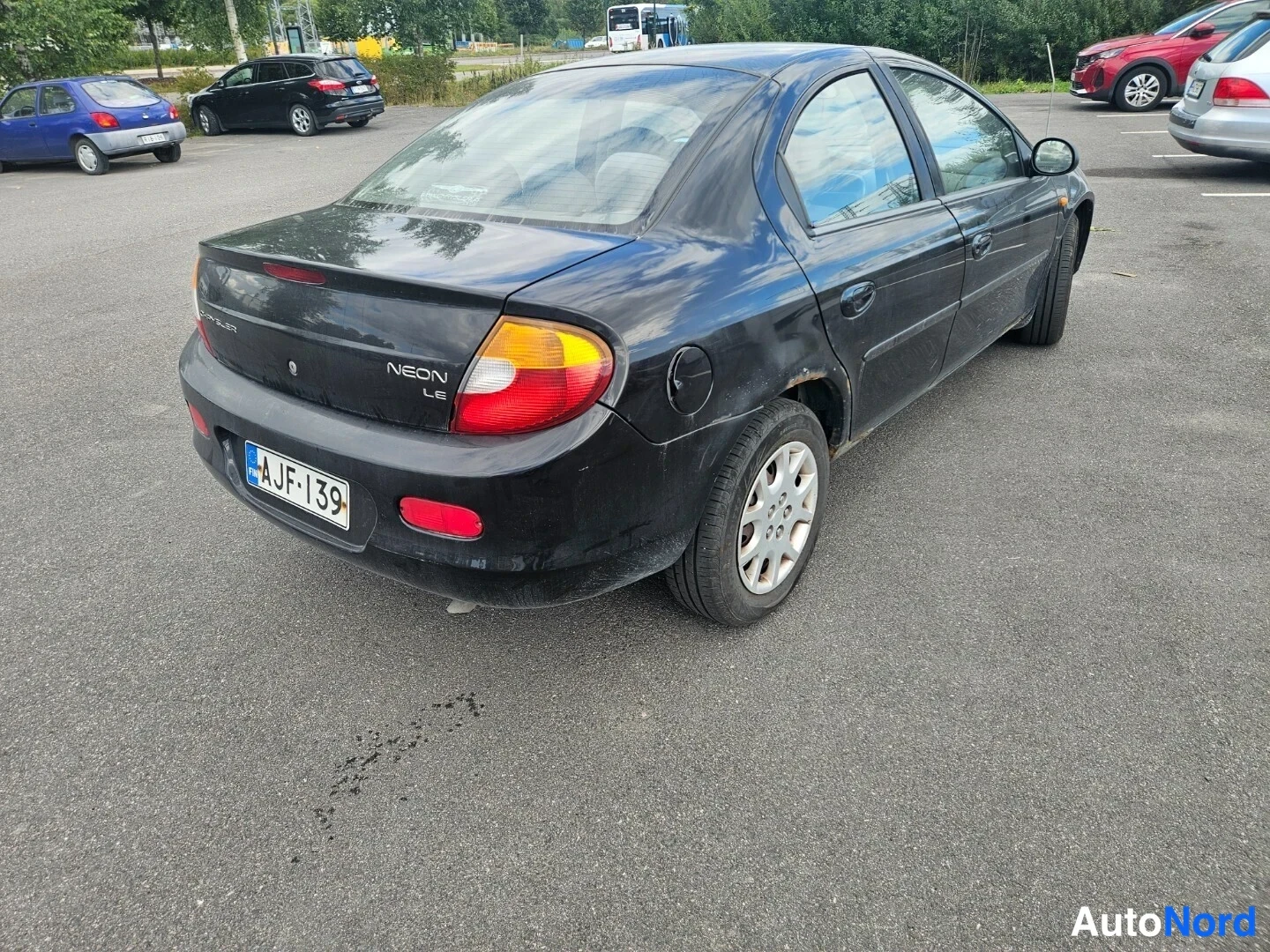Takaviisto: Musta Chrysler Neon takakulmasta oikealta, NEON-merkintä perällä ja -tunnus näkyvät parkkipaikalla.
