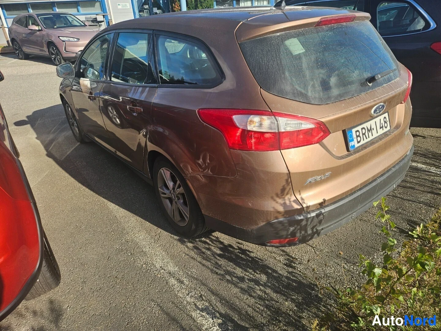 Takaviisto: Ruskean Ford Focus -farmarin takakulmakuva vasemmalta, rekisterikilpi, takakannen Focus-teksti ja takatuulessa seisova auto.