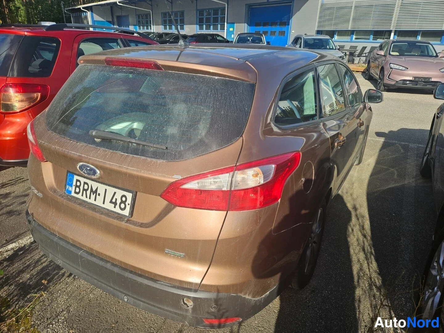 Takaviisto: Ruskean Ford Focus -farmarin takanäkymä oikealta, rekisterikilpi, takalasinpyyhkijä ja korin sivussa pintanäreitä.
