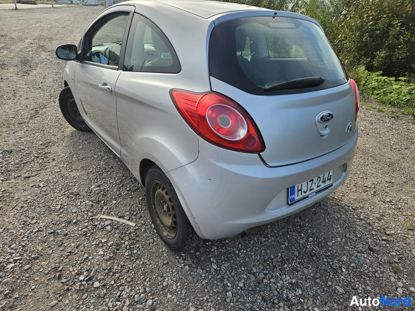 Takaviisto: Hopeanvärinen Ford Ka takaa ja vasemmalta päin kuvattuna sorapohjaisella paikalla, punaiset takavalot ja rekisteri näkyvät.
