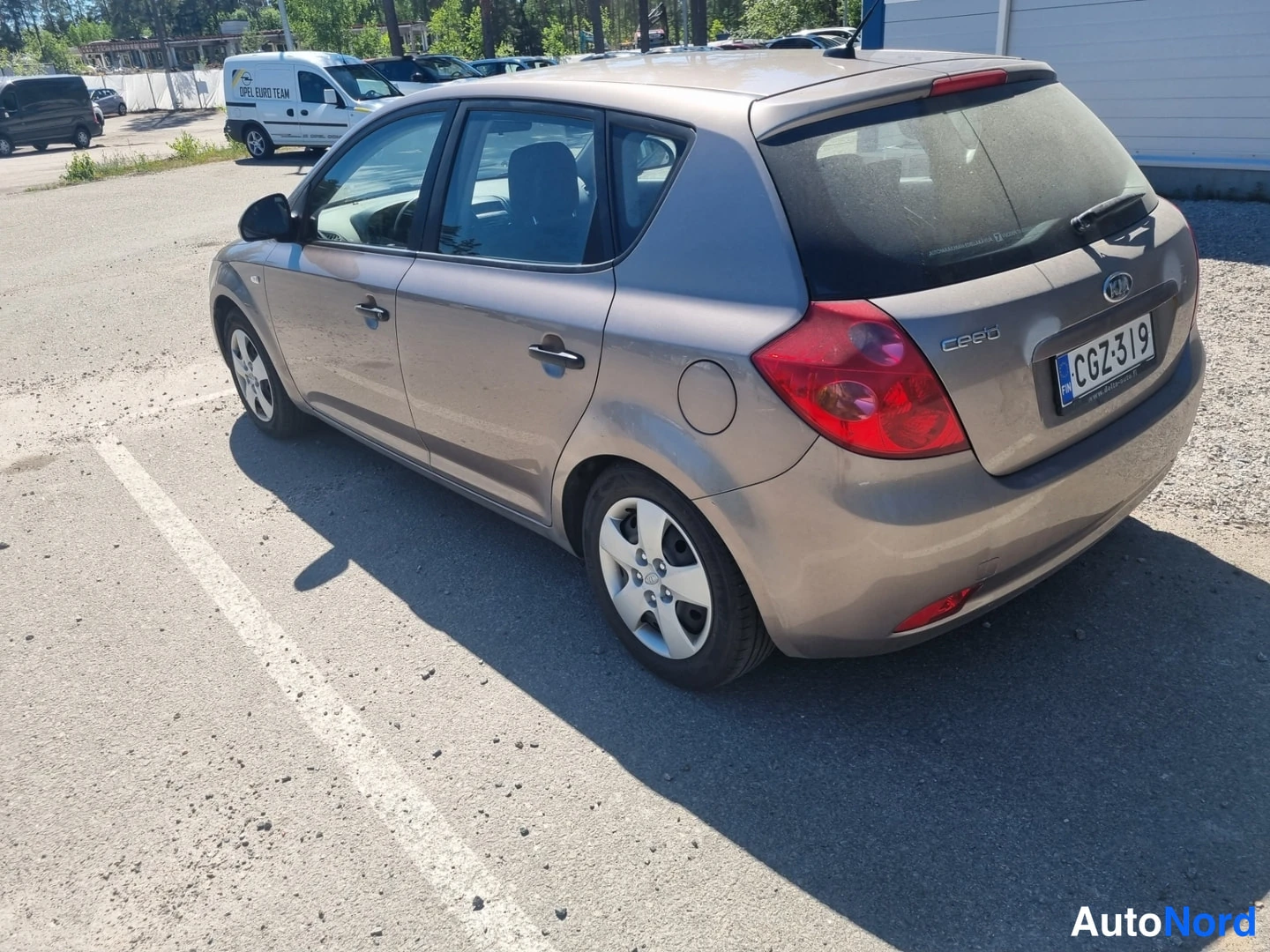 Takaviisto: Kia Ceed viistosti takaa vasemmalta kuvattuna ruskeanharmaalla maalilla; rekisterikilpi ja takavalot näkyvät.