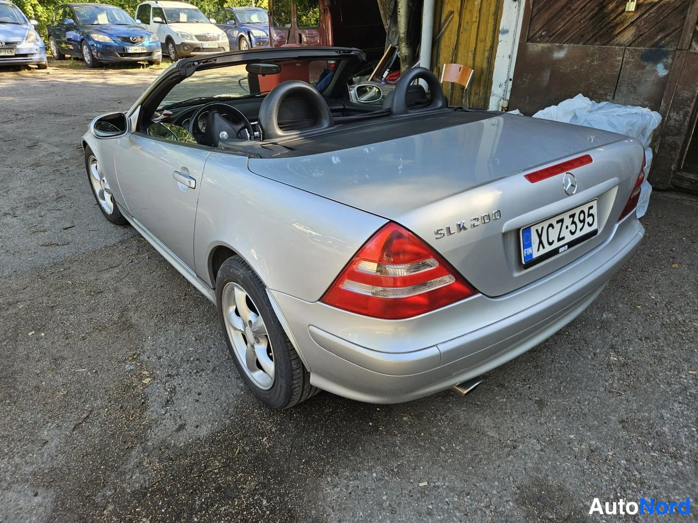 Takaviisto: Hopeanvärinen Mercedes SLK 200 takakulmasta oikealta, rekisteritunnus, SLK 200 -merkintä kannessa.