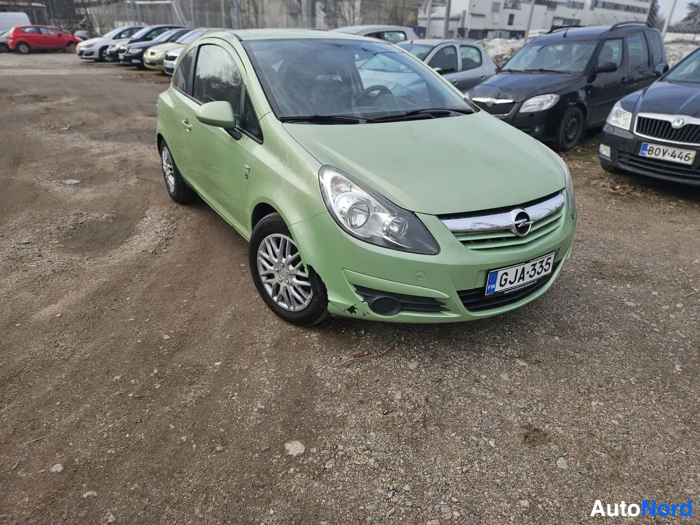 Etuviisto, nokka oikealle: Vaaleanvihreä Opel Corsa etuosa kolmesta neljäsosasta, keula oikealla, rekisterikilpi luettavissa.
