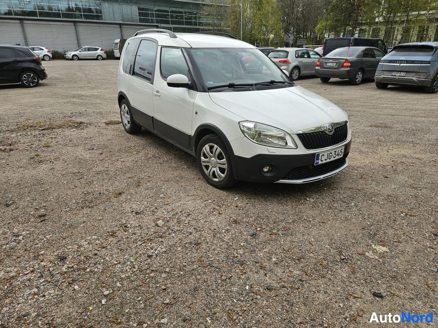 Etuviisto, nokka oikealle: Valkoinen tilavautomobiili kolmesta neljäsosakulmasta, keulanosa ja molemmat kyljet näkyvissä, mustat muovilistat ja kattokaaret.