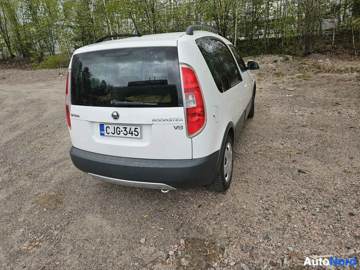 Takaviisto: Valkoinen tilavautomobiili takaa kolmesta neljäsosakulmasta, perä ja kylki näkyvissä, takaluukussa merkinnät Skoda Roomster ja V8.