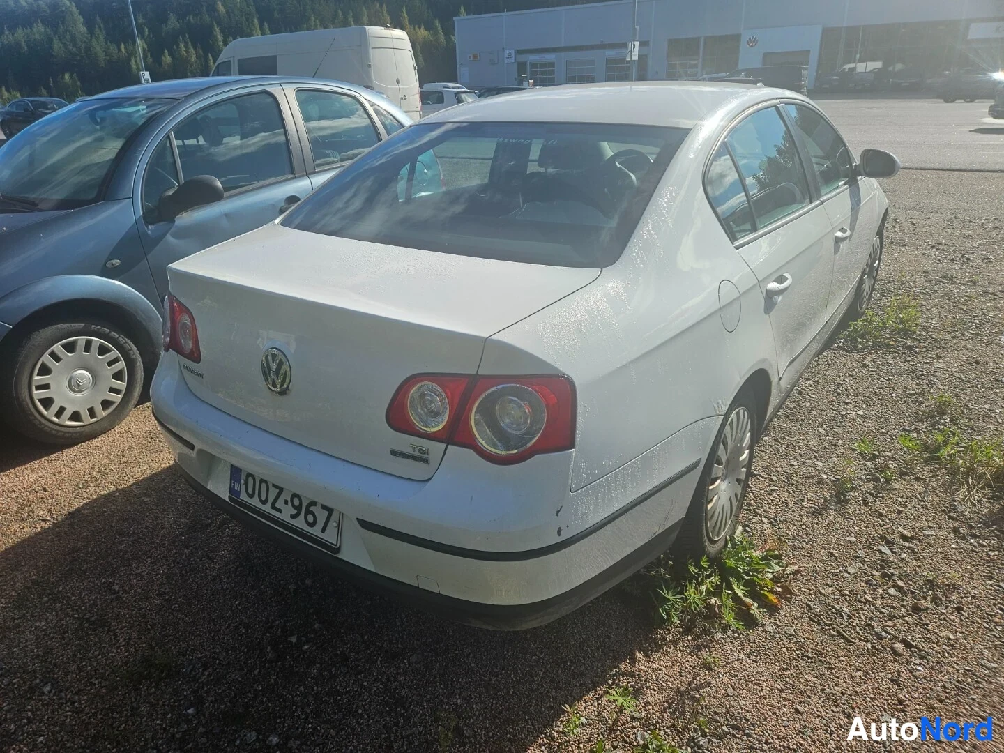 Takaviisto: Valkoinen Volkswagen Passat -henkilöauto takaosalta ja oikealta sivulta kuvattuna paikoitusalueella.