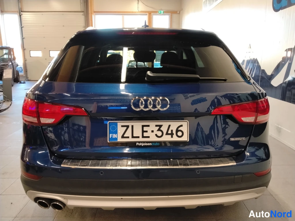 Takaa: Sininen farmariauto sisätiloissa suoraan takaa nähtynä, rekisteritunnus ja kahdet pakoputket.