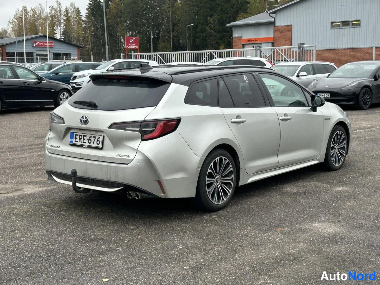 Takaviisto: Toyota Corolla -farmari takaa-oikealta kuvattuna, hopeinen koriväri, rekisterikilpi, peräosassa HYBRID-merkintä ja kytketaimu.