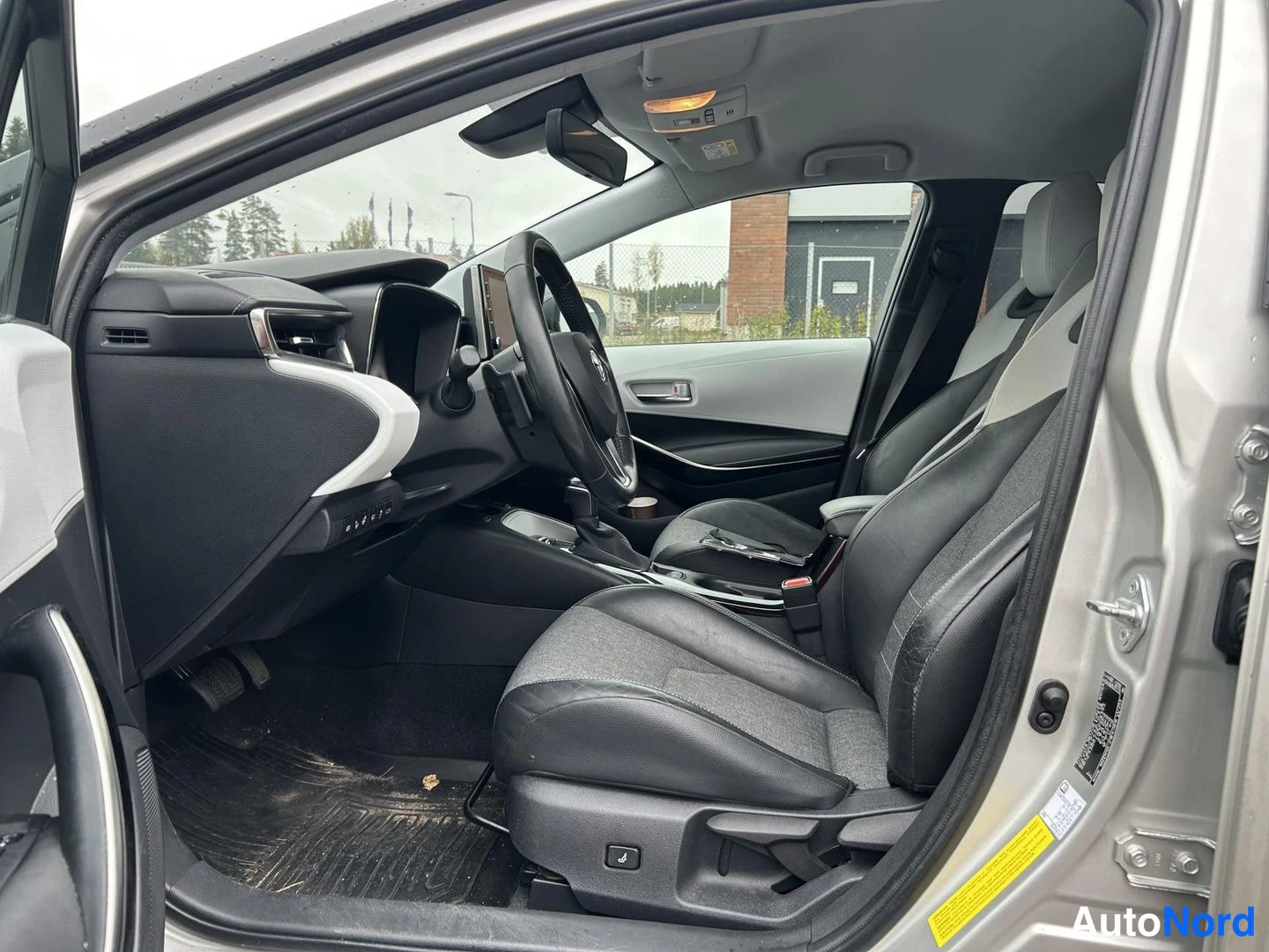 Muu: Toyota Corolla:n etumatkustustila kuljettajan ovesta kuvattuna: mustat istuimet, ohjauspyörä ja kojelauta.